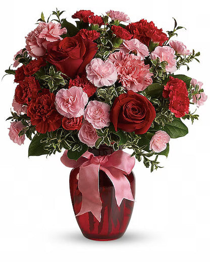 Red and pink floral bouquet in a red vase with a pink ribbon, sitting on a clean white tabletop