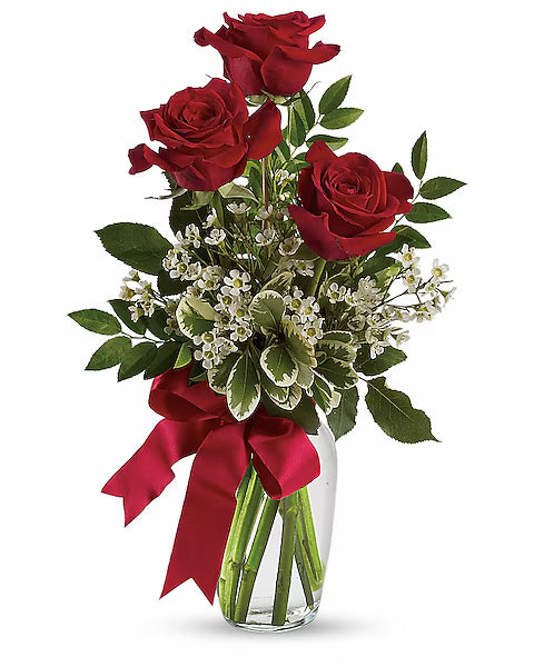 Bouquet of red roses with green leaves and a red bow in a clear vase